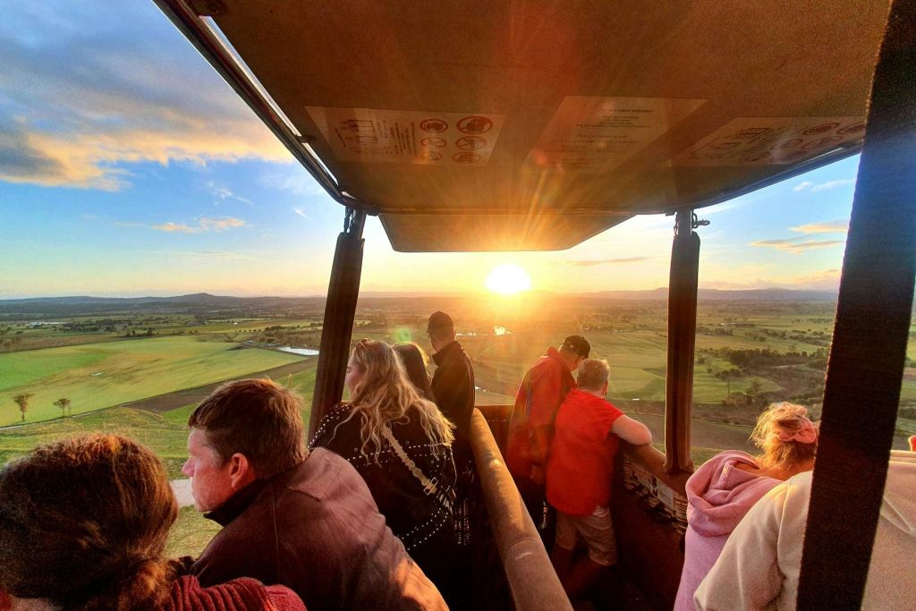 열기구 바구니를 든 사람들은 해가 지는 동안 광활한 녹색 풍경의 전망을 즐깁니다.