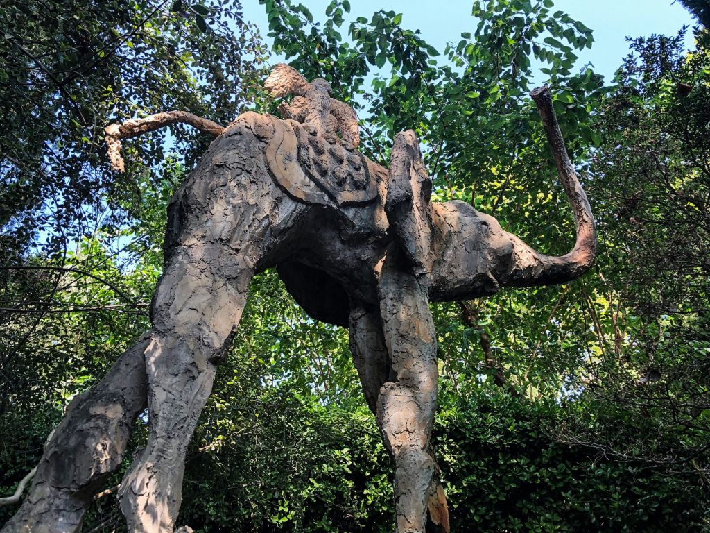 빽빽한 녹색 단풍과 나무로 둘러싸인 사람이 타고 있는 코끼리의 진흙 조각상.