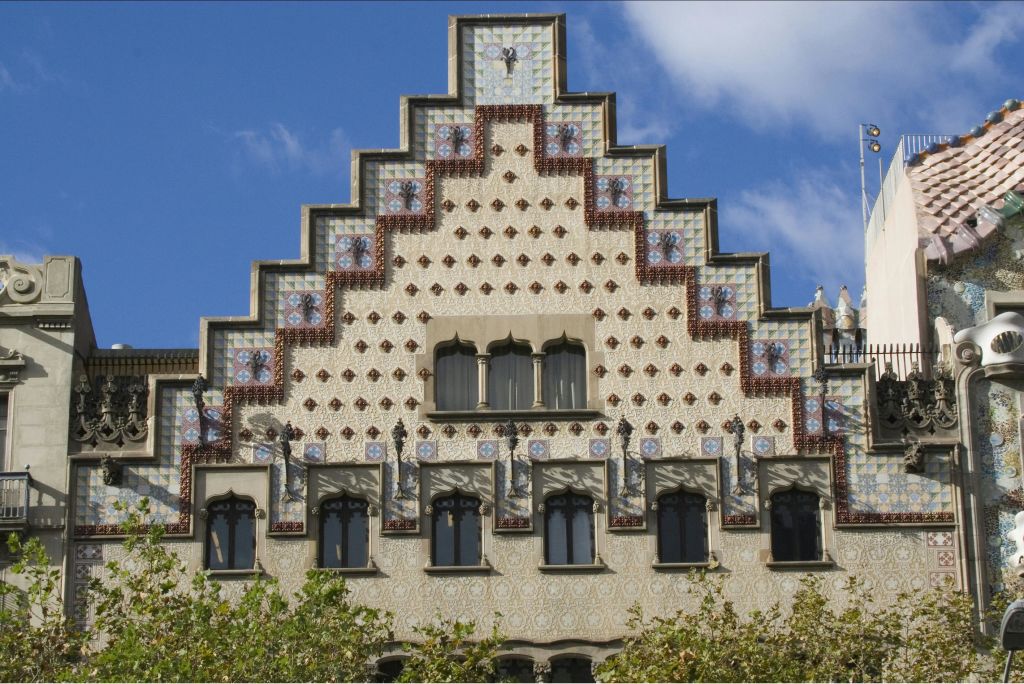 파란 하늘을 배경으로 무늬 타일, 아치형 창문, 계단식 지붕 디자인이 돋보이는 화려한 건물 외관.