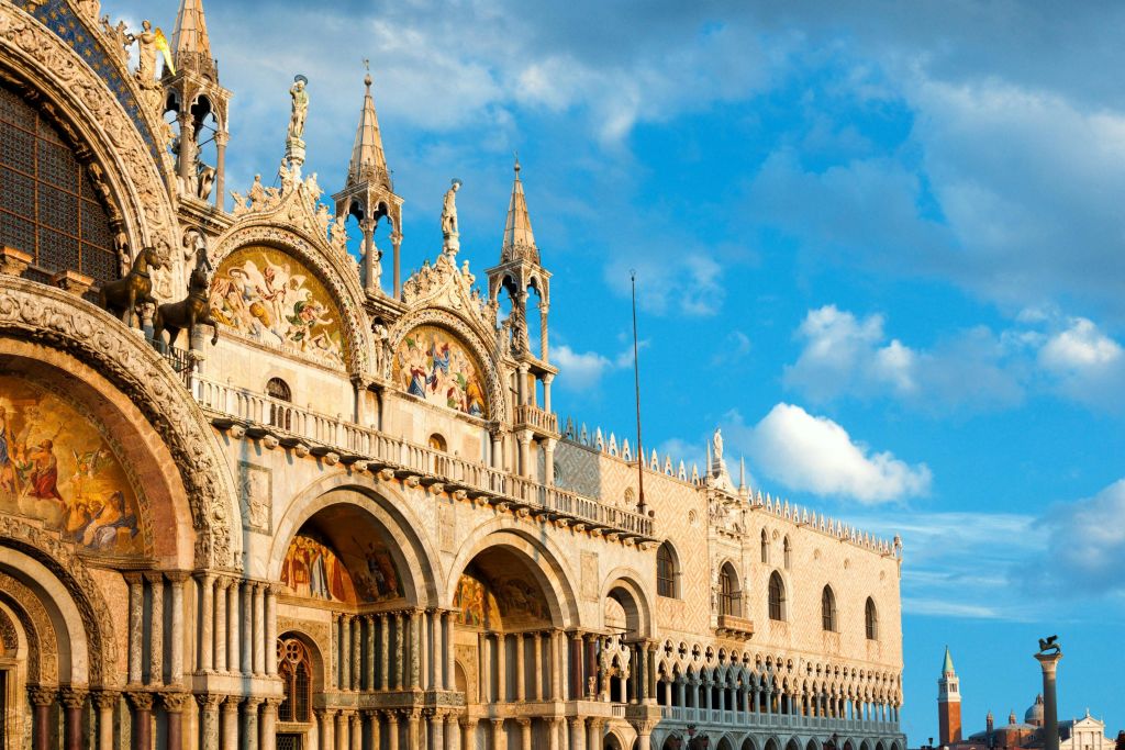 푸른 하늘 아래 흩어져 있는 구름과 함께 아치, 정교한 조각, 동상, 모자이크 작품이 있는 화려하고 유서 깊은 건물.