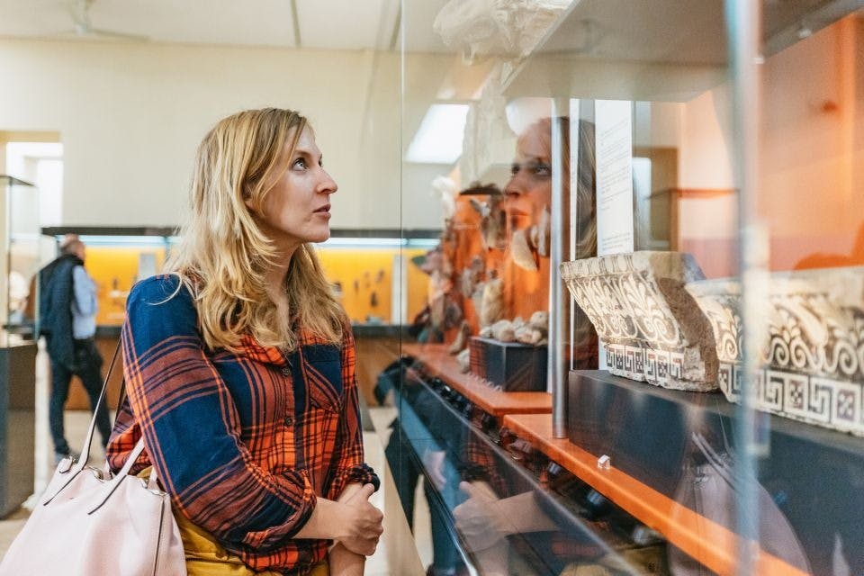 격자 무늬 셔츠를 입은 여성이 박물관 진열 케이스의 전시물을 배경으로 다른 방문객들과 함께 관람하고 있습니다.