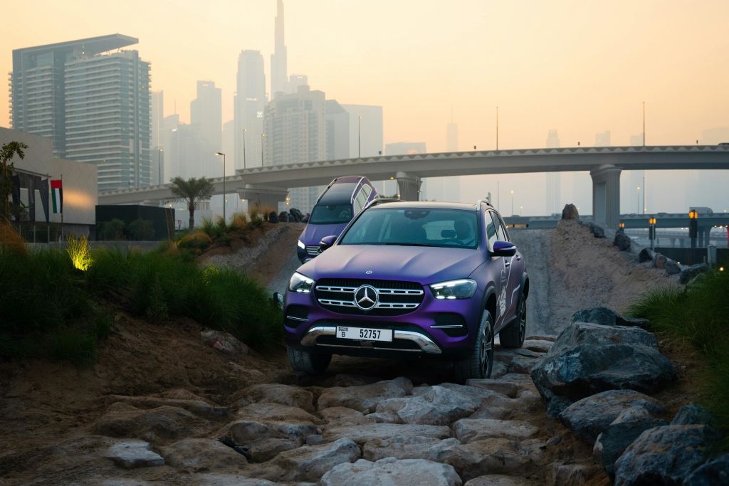 석양을 배경으로 도시 풍경과 고속도로 다리가 있는 바위길에서 즐기는 메르세데스 SUV.