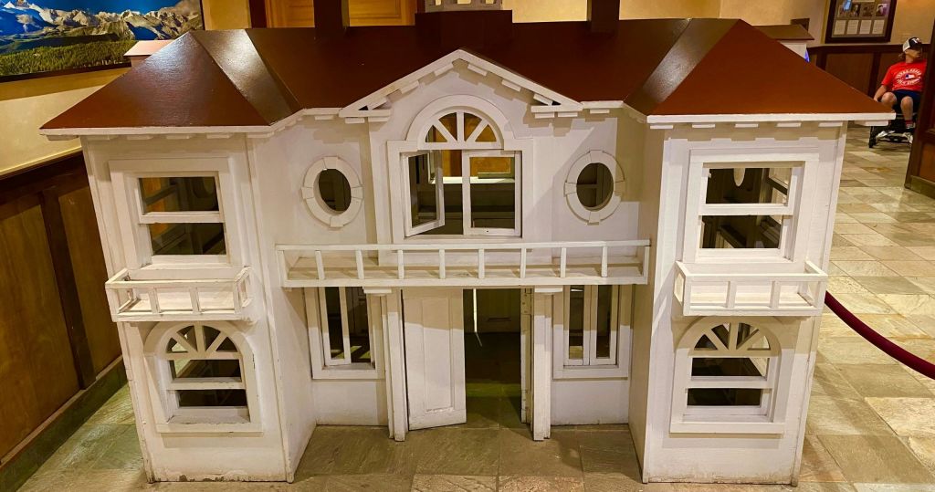 빨간색 지붕, 원형 창문, 실내 타일 바닥에 작은 발코니가 있는 미니어처 흰색 목조 주택입니다.