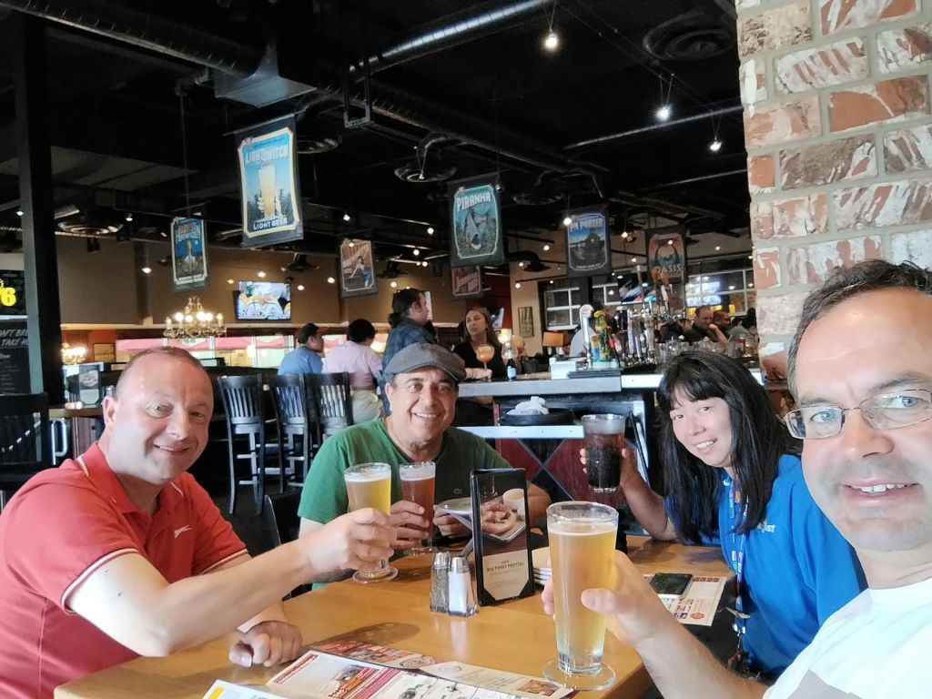 4명이 레스토랑 테이블에 앉아 미소를 짓고 음료를 들고 있습니다. 배경에는 다른 후원자와 바 영역이 표시됩니다.