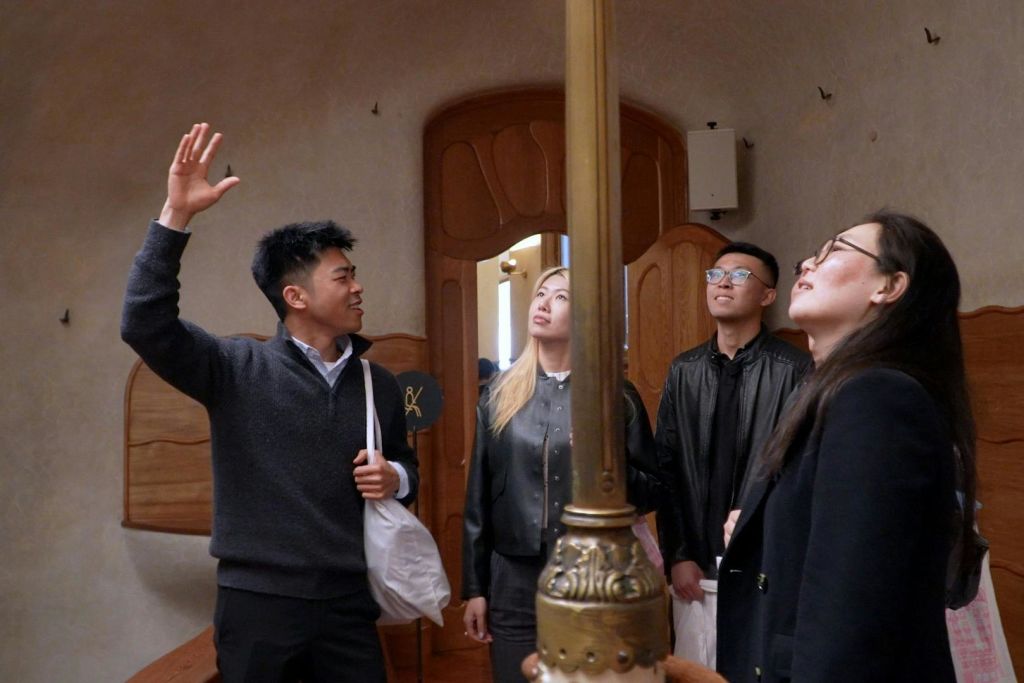 한 사람이 나무와 황동의 건축적 요소가 돋보이는 실내 환경에서 다른 사람들과 어울리며 위를 향해 제스처를 취합니다.