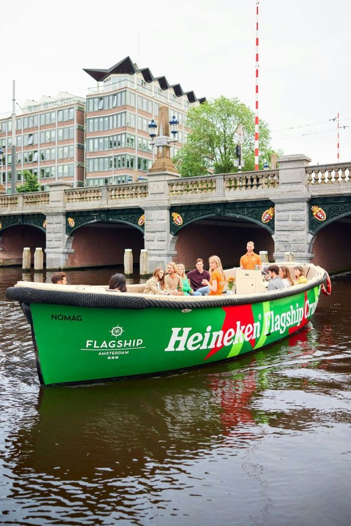 관광객들은 암스테르담에서 운하 보트 투어를 즐기며 보트에 '하이네켄 플래그십 (Heineken Flagship)' 브랜드가 새겨진 다리 아래를 지나갑니다.