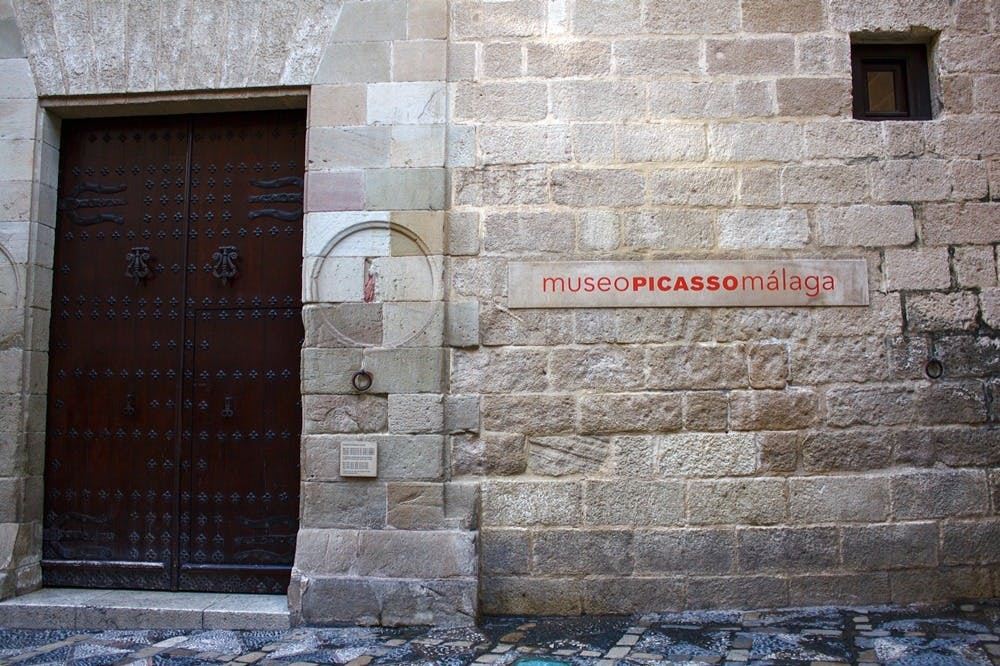 나무 문과 "museo PICASSO málaga" 라고 적힌 간판이 있는 돌담.