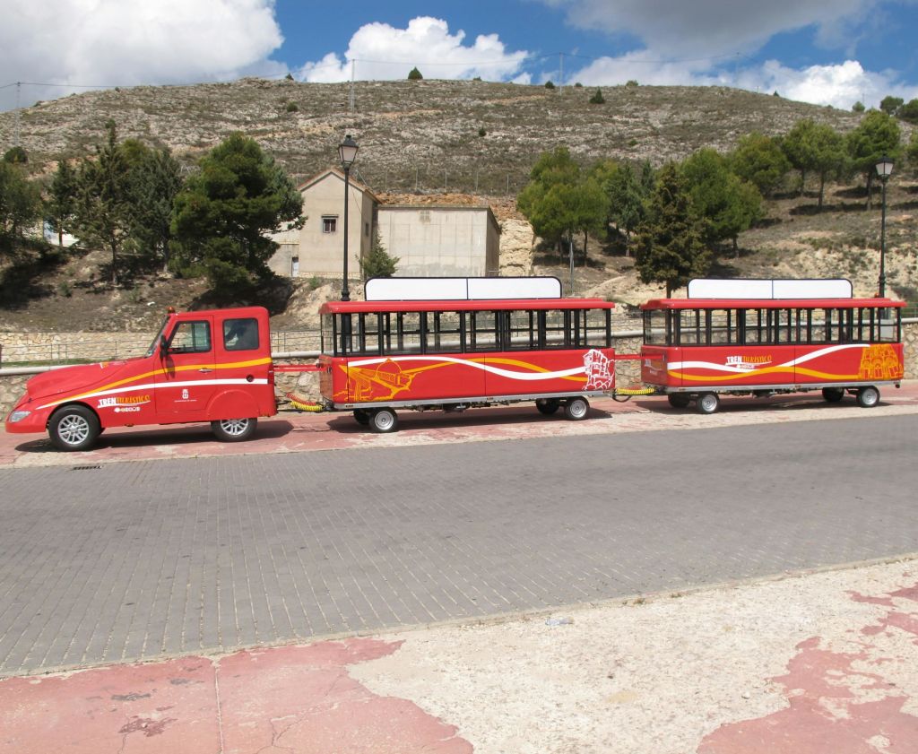 나무와 언덕 풍경을 배경으로 포장 도로에 연결된 마차 두 대가 주차된 빨간색과 노란색의 관광 열차.