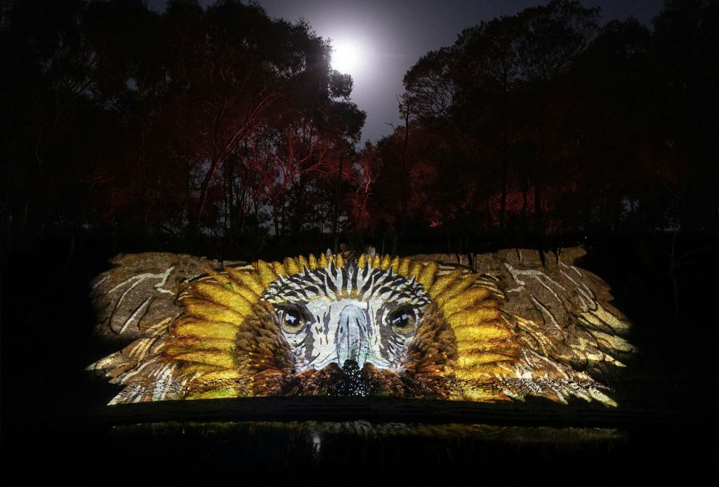 보름달과 실루엣 나무를 배경으로 바위 풍경에 커다랗고 빛나는 독수리 얼굴이 투영됩니다.