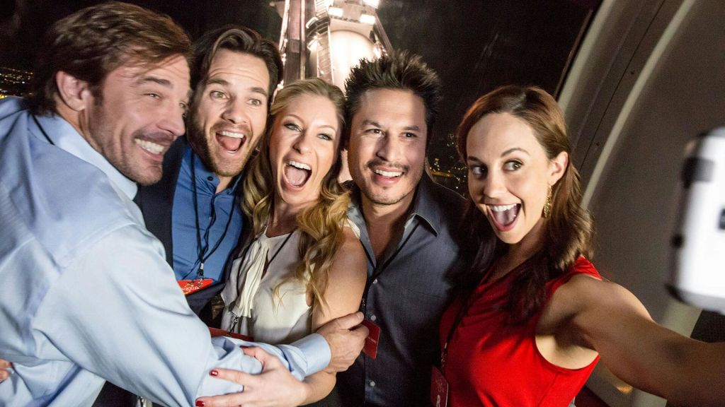 끈이 달린 5명이 밤이 되면 불이 켜진 구조물을 배경으로 단체 사진 촬영을 위해 신나게 포즈를 취하고 미소를 짓고 있습니다.