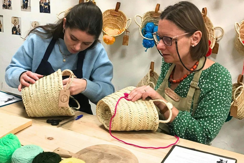 안경을 쓰고 초록색 물방울무늬 셔츠를 입은 한 여성이 빨간색 원사를 짚 바구니에 넣고 매달린 바구니로 둘러싸고 있습니다.