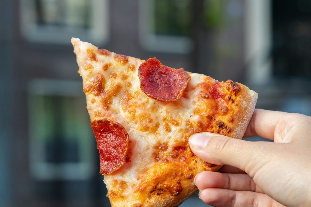 야외 배경이 흐릿한 페퍼로니 피자 조각을 들고 있는 손.