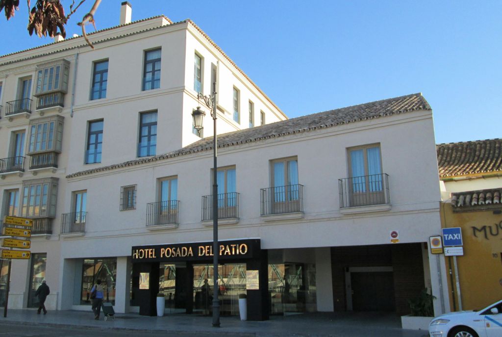 여러 개의 창문, 발코니, 입구 근처의 "Hotel Posada del Patio" 표지판이 있는 크림색 건물의 외관.