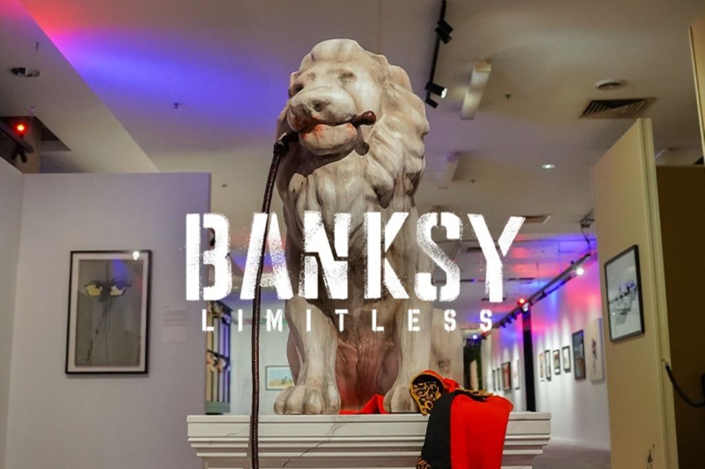 아트 갤러리에 전시된 받침대에 'BANKSY LIMITLESS' 라는 글자가 이미지에 겹쳐진 사자상.