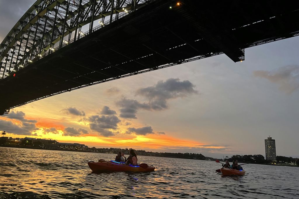 석양의 시드니 하버 브리지 아래 카약 타는 사람들