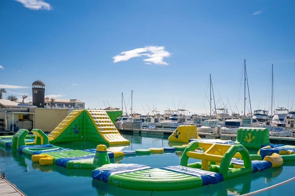 미끄럼틀과 장애물이 물 위에 떠 있는 풍선 워터파크에는 맑은 하늘 아래 보트가 가득한 정박지가 있습니다.