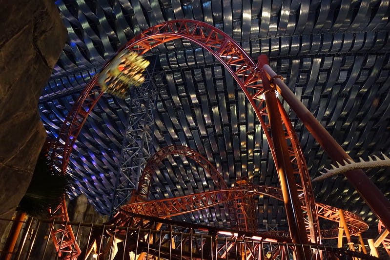 늑골이 있는 금속 지붕 아래 고리가 있는 빨간색 롤러코스터로, 움직이는 흐릿한 열차가 특징입니다.