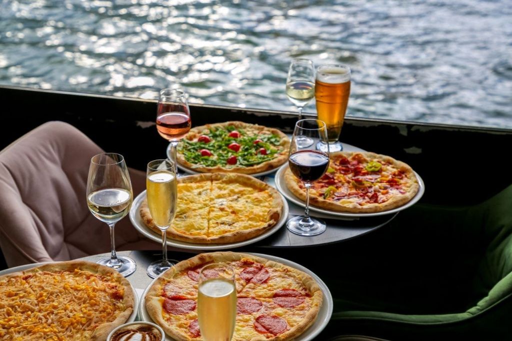 5개의 피자와 와인과 맥주를 포함한 다양한 음료가 물을 배경으로 테이블에 준비되어 있습니다.