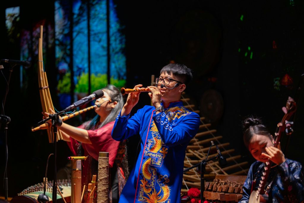 전통 복장을 한 뮤지션들은 무대에서 숲을 배경으로 다양한 악기를 연주합니다.