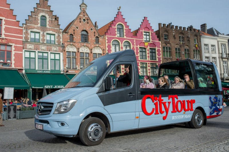 자갈길의 화려한 역사적 건물 앞에서 승객을 태우고 "시티 투어" 브랜딩이 있는 투어 버스.