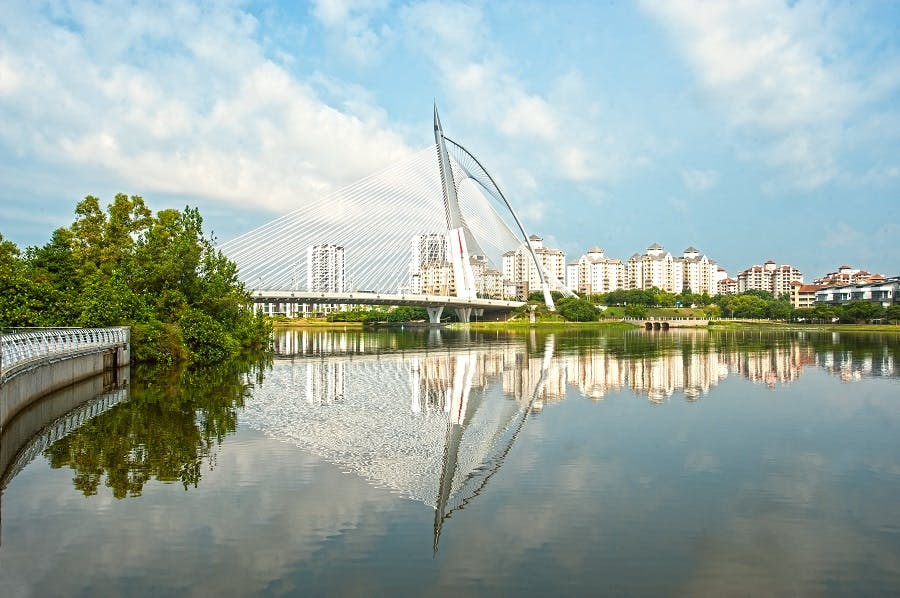 푸른 하늘 아래 물속의 다리와 도시 건물이 반영된 잔잔한 강 위의 현수교.