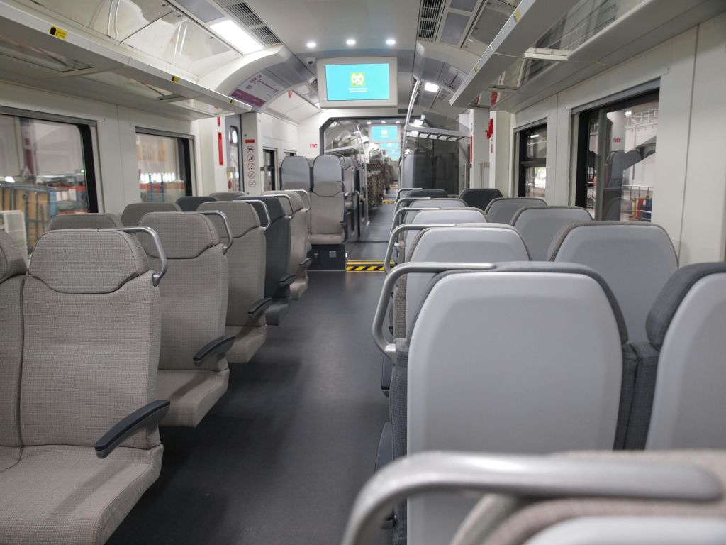 회색 좌석, 머리 위 수하물 선반, 로고와 파란색 배경이 표시된 스크린이 있는 빈 열차 마차의 내부.