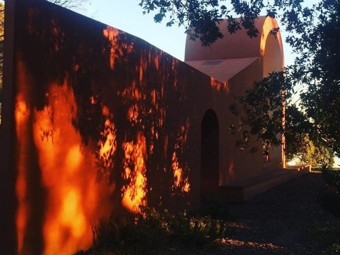 햇살은 나뭇가지로 둘러싸인 아치형 출입구가 있는 오렌지색 치장 벽토 건물에 나뭇잎 그림자를 드리웁니다.