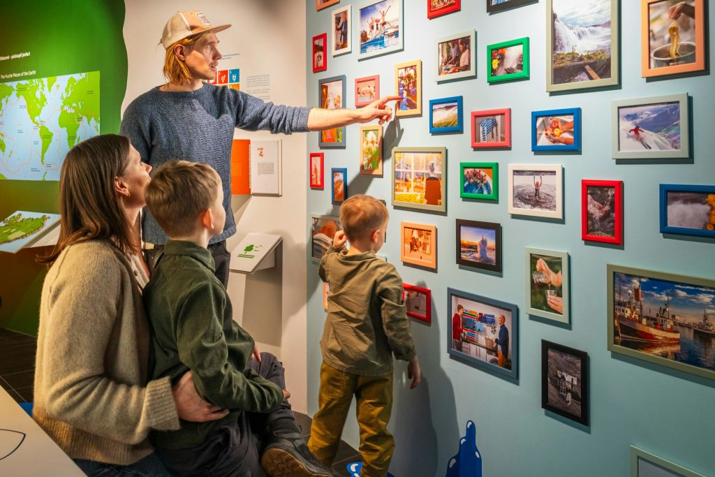 4인 가족이 다양한 액자 그림이 있는 갤러리 벽을 살펴봅니다. 지도와 디스플레이가 배경에 표시됩니다.