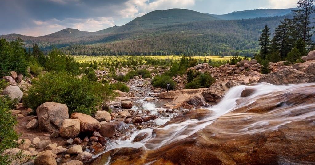 바위 사이로 흐르는 시냇물이 흐르는 산 풍경과 물가에 사람이 서 있는 풍경.