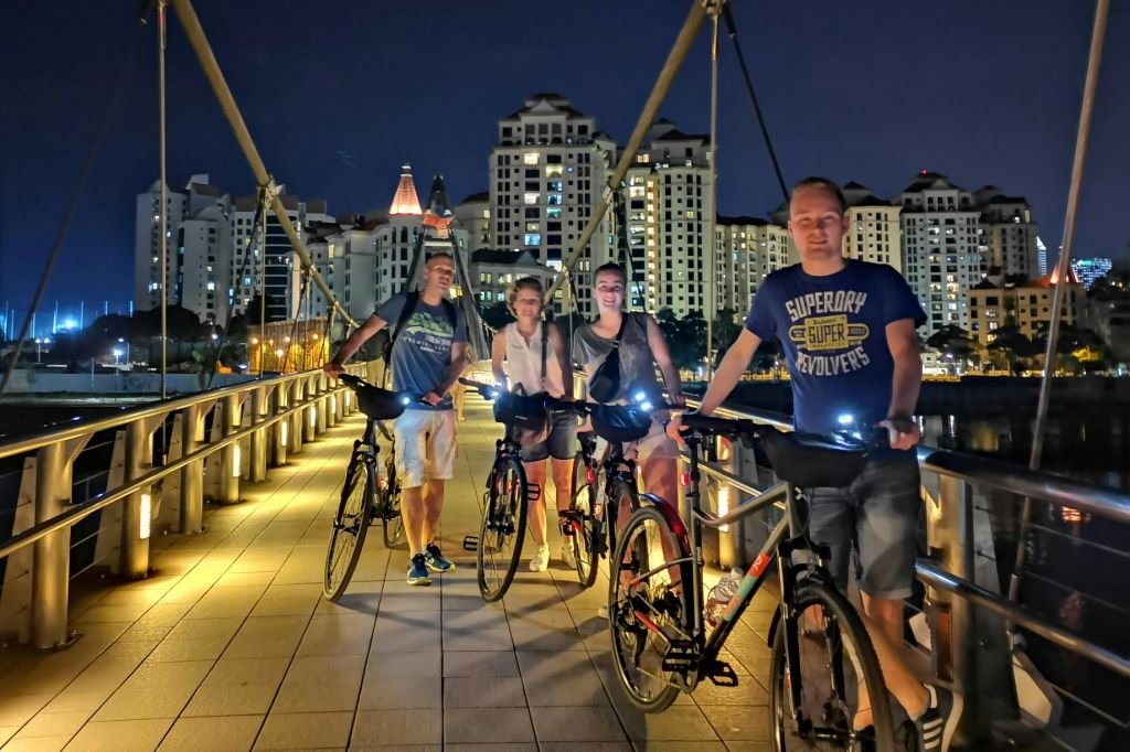 밤에는 다리에 자전거를 탄 4명의 사람들이 도시 건물을 배경으로 불을 밝힙니다.