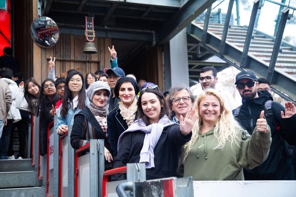 빨간색 케이블 철도를 기다리는 사람들은 모두 카메라를 향해 손을 흔들거나 미소를 짓고 있습니다.