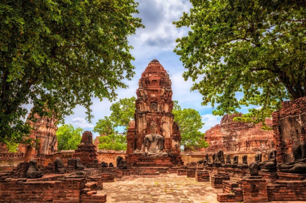 부분적으로 흐린 하늘 아래 녹지와 나무로 둘러싸인 유서 깊은 사원 유적지.