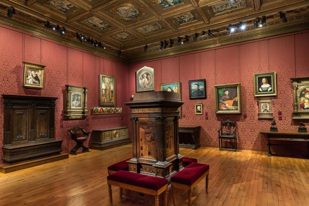 붉은 벽, 나무 바닥, 화려한 천장이 있는 아트 갤러리입니다. 다양한 액자 그림과 클래식 가구가 전시되어 있습니다.