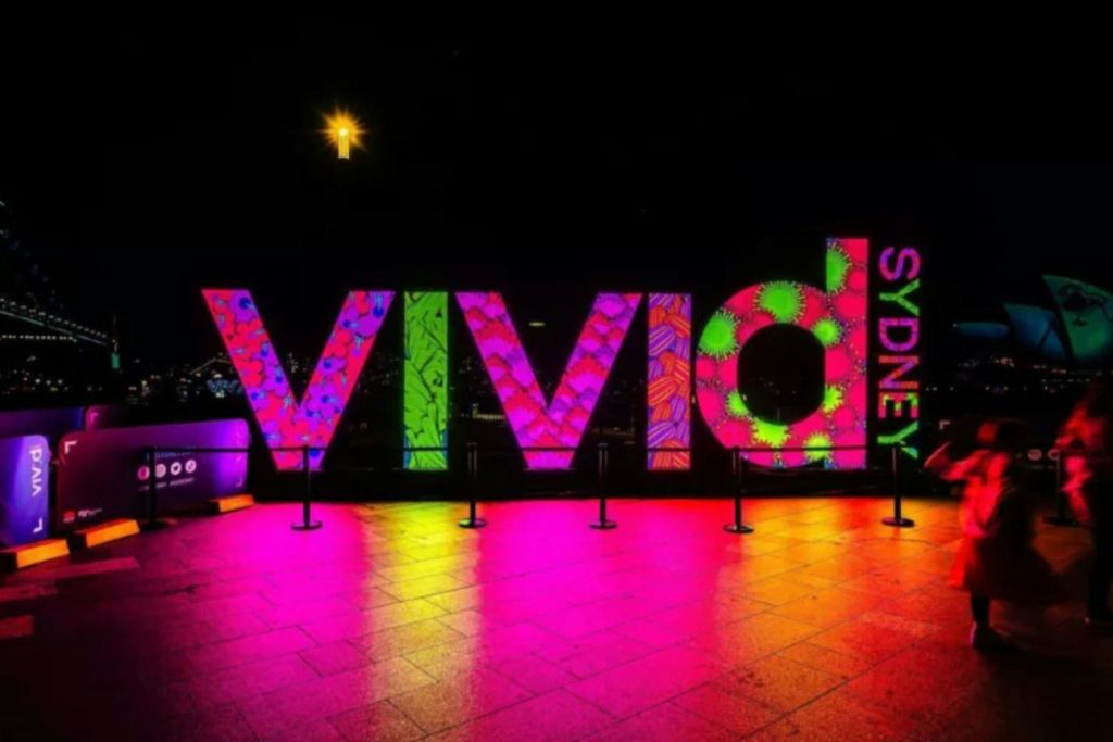 어두운 배경에 화려한 패턴과 조명이 밝은 '비비드 시드니 (Vivid Sydney)' 표지판입니다.