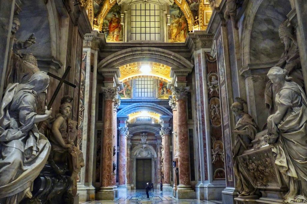아치, 기둥, 조각상, 정교한 천장 디테일이 돋보이는 웅장한 건물의 화려한 인테리어와 산책하는 사람.