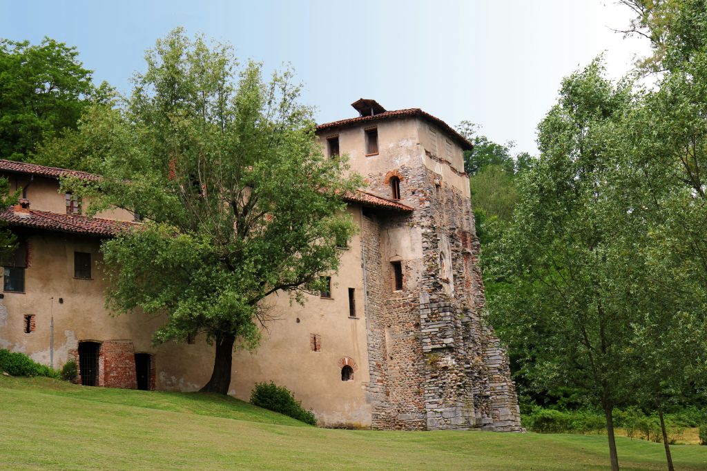 타일로 마감된 지붕과 부분적으로 폐허가 된 벽, 나무와 잔디밭으로 둘러싸인 고대 석조 건물이 맑은 하늘 아래 있습니다.