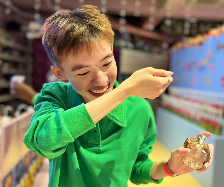 초록색 셔츠를 입은 사람이 다채롭고 초점이 맞지 않는 배경 요소로 숟가락을 입에 대고 미소를 짓고 있습니다.