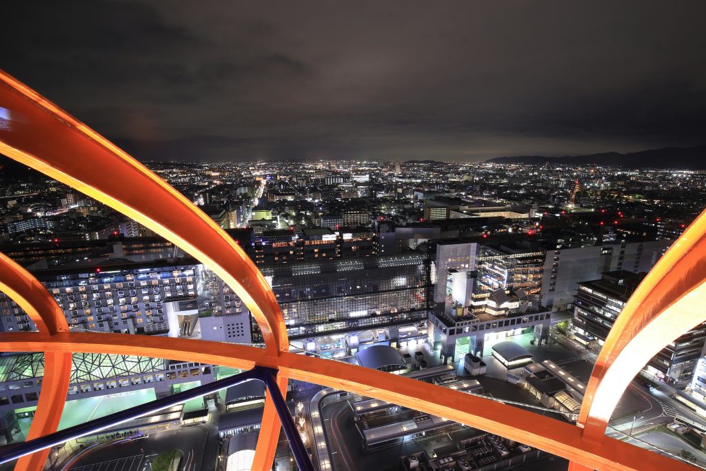 주황색 금속 구조물을 통해 위에서 볼 수 있는 조명 건물과 거리가 있는 야간 도시 풍경.