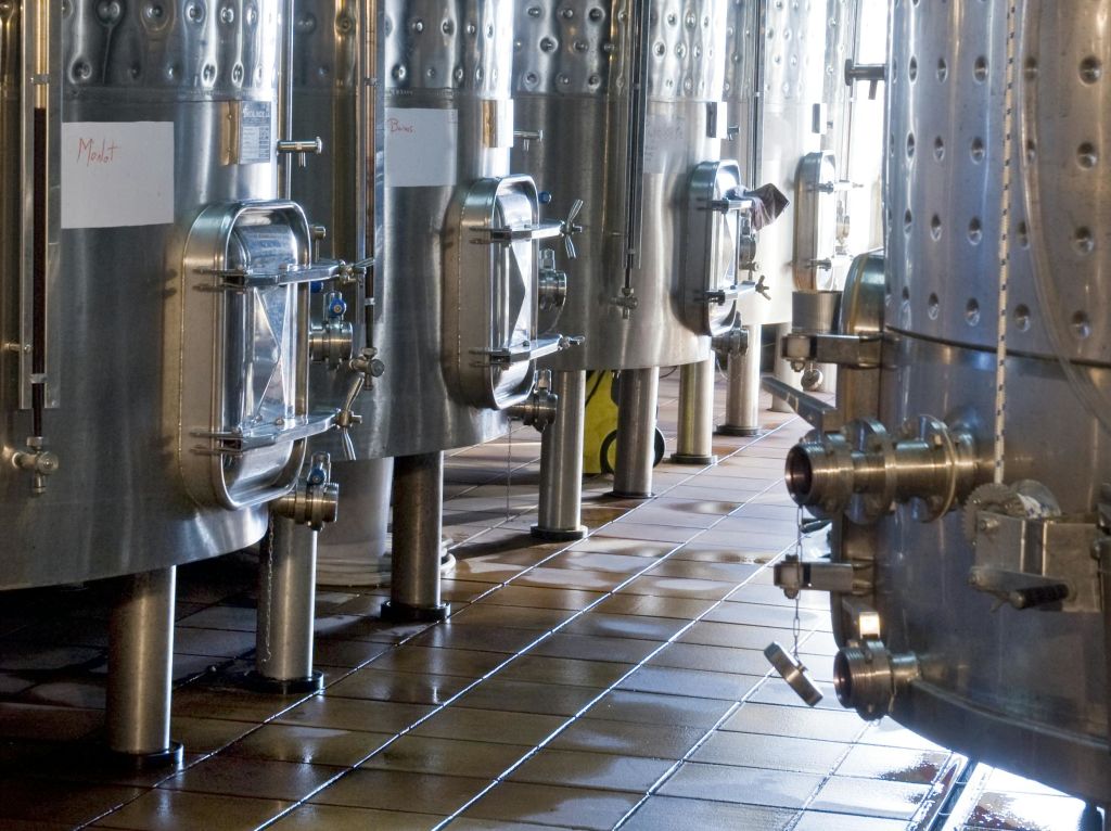 타일 바닥에 유리 해치와 밸브가 있는 대형 스테인리스 스틸 탱크 (양조장 또는 산업 시설에 있을 수 있음).