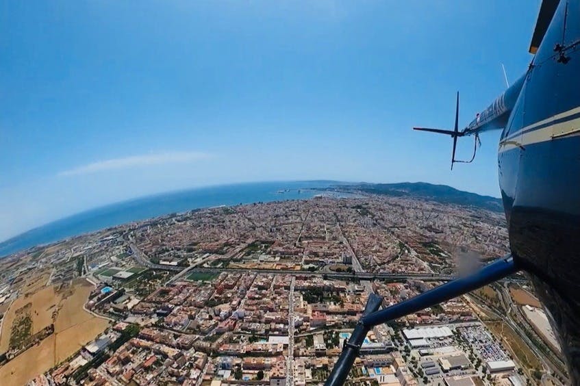 맑고 푸른 하늘 아래, 빽빽한 건물과 헬리콥터 로터가 보이는 해안 도시의 공중 전망.