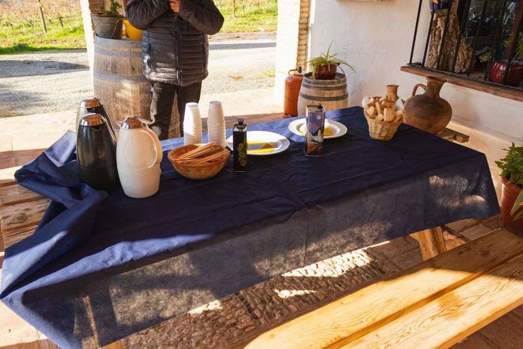 커피 카라페, 컵, 접시, 올리브 오일 병, 빵 바구니, 식기가 놓인 테이블입니다. 배경에 서 있는 사람.