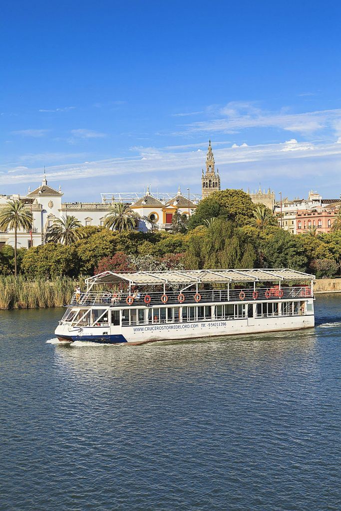 푸른 하늘 아래 울창한 나무와 유서 깊은 건물, 높은 교회 타워를 배경으로 하얀 보트를 타고 강을 둘러보세요.