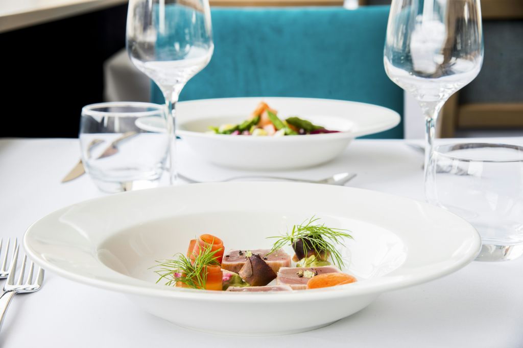 화이트 테이블 위에 고기, 당근, 채소를 썰어 우아하게 플레이팅한 요리, 와인잔과 다른 요리를 배경으로 한 세트.