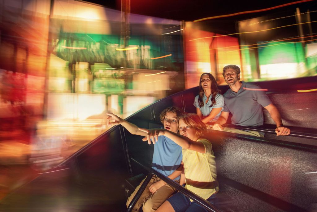 4인 가족이 다채롭고 흐릿한 조명을 배경으로 실내 놀이기구를 신나게 타고 있습니다.