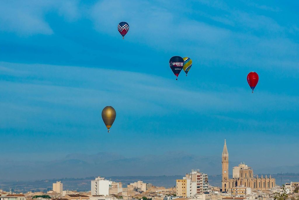 저명한 교회 타워가 있는 도시 풍경 위로 밝고 푸른 하늘에 여러 개의 열기구가 떠 있습니다.