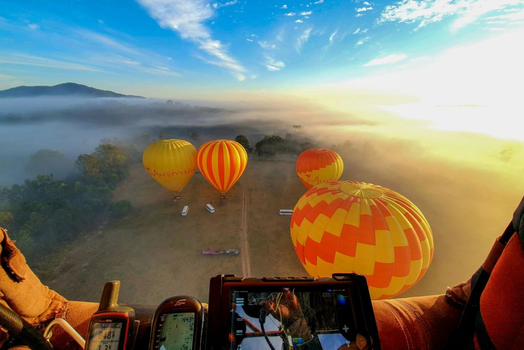 해가 뜰 때 안개 낀 들판 위로 열기구가 떠 있습니다. 제어판과 기기가 전경에 보입니다.