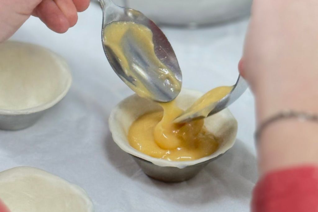 한 사람이 숟가락을 사용하여 노란색 충전재로 페이스트리 껍질을 채우고 있습니다.