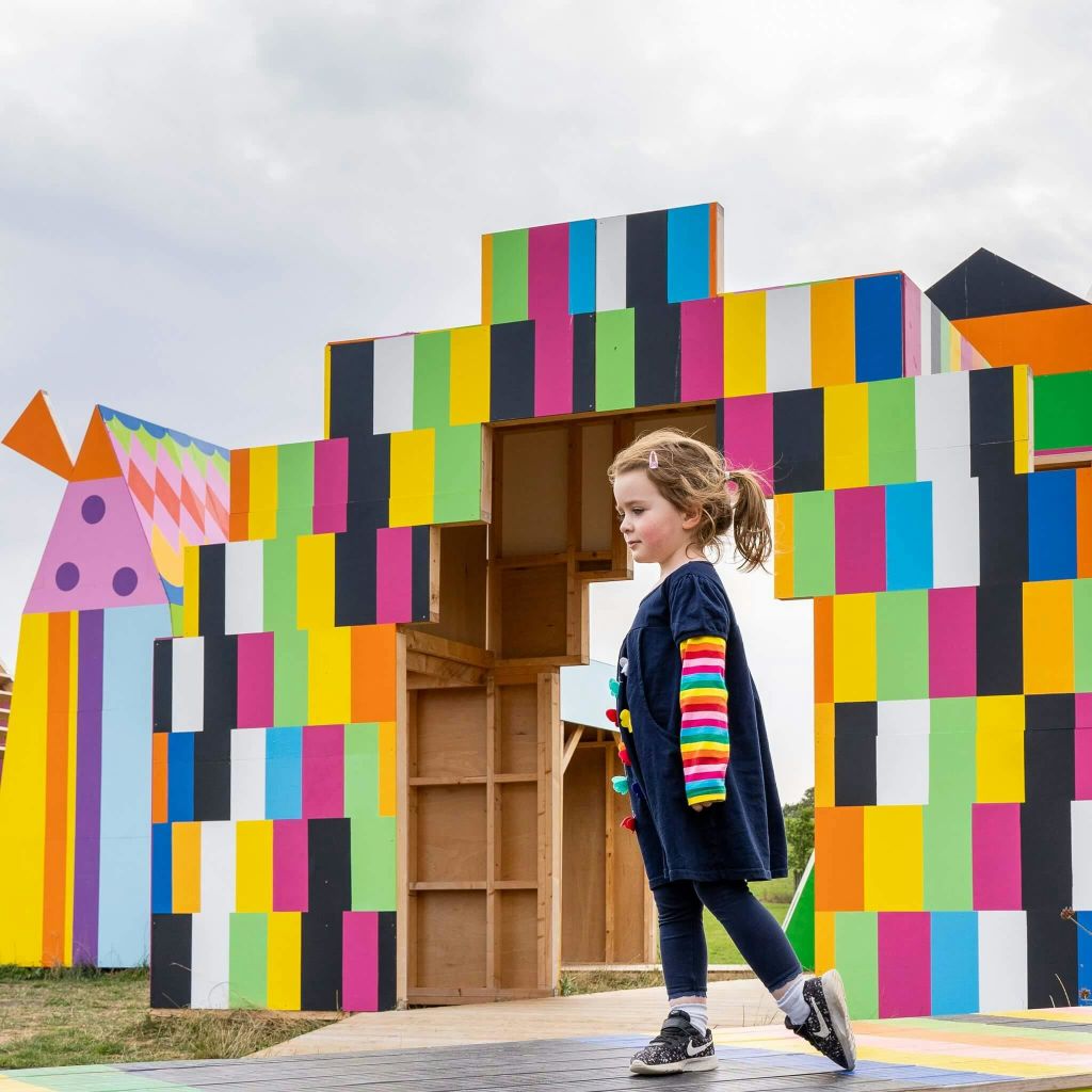한 어린이가 탁한 하늘 아래 야외에 있는 크고 화려한 블록 구조물 앞을 걷고 있습니다.