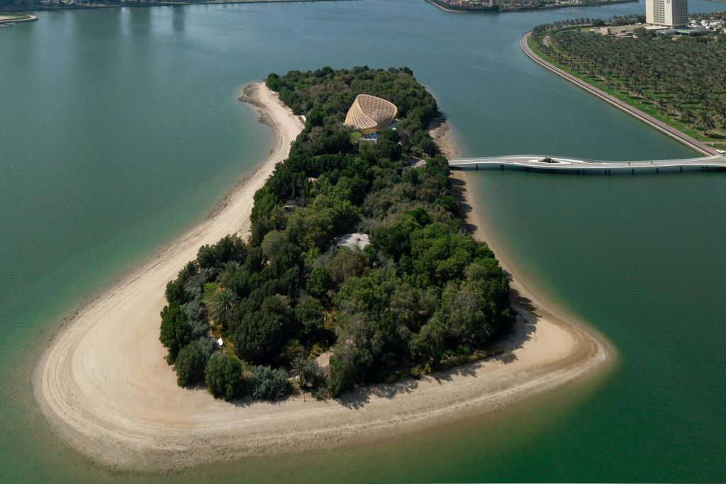 돔 모양의 건물, 모래 해변, 본토와 연결되는 다리가 있는 울창하고 숲이 우거진 섬의 공중 전망.