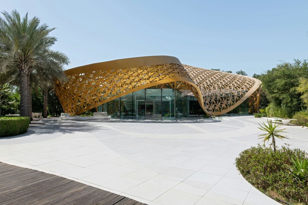 맑고 푸른 하늘 아래 독특한 곡선 격자 무늬의 황금 지붕과 유리 벽이 있는 현대적인 건물입니다.